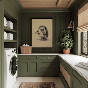 A whimsical sketch of a hedgehog with toilet paper playfully graces this vintage bathroom, framed in black and surrounded by lush green cabinetry, a woven basket, and ambient lighting.