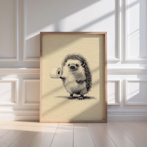 A whimsical hedgehog sketch humorously holding a toilet roll is elegantly framed in light wood, casting gentle shadows in a minimalist bathroom, perfect for adding retro wall art charm to your bathroom decor.
