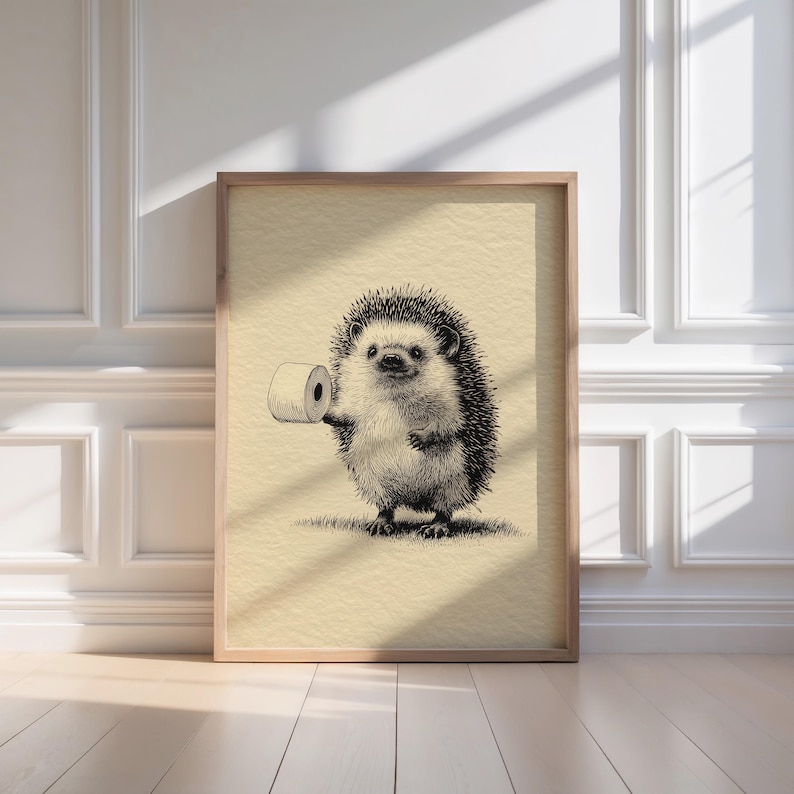 A whimsical hedgehog sketch humorously holding a toilet roll is elegantly framed in light wood, casting gentle shadows in a minimalist bathroom, perfect for adding retro wall art charm to your bathroom decor.
