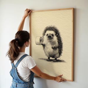 A woman hangs a whimsical hedgehog art print in a simple wooden frame, adding a playful and humorous touch to the funny bathroom wall decor.