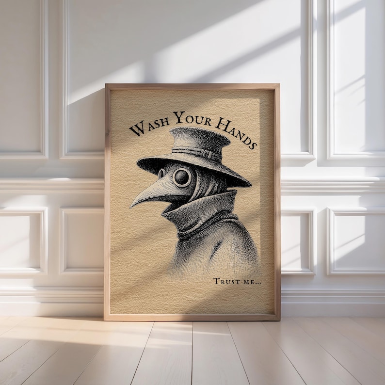 A stylish wooden frame elegantly showcases the spooky plague doctor art with "Wash Your Hands" in bold, positioned against a clean, white-paneled wall, perfect for moody bathroom decor. 

Sunlight filters through, casting intriguing shadows on this whimsical and dark academia-inspired bathroom wall art.