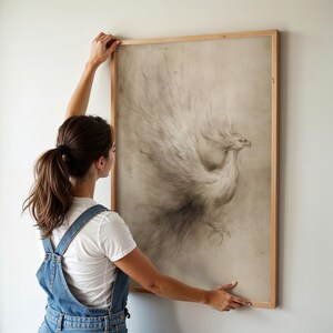 A delicate phoenix sketch in a vintage frame is gently placed on a light-toned wall, creating a whimsical fantasy decor accent. The airy room with soft lighting enhances the elegance of this nerdcore art piece.