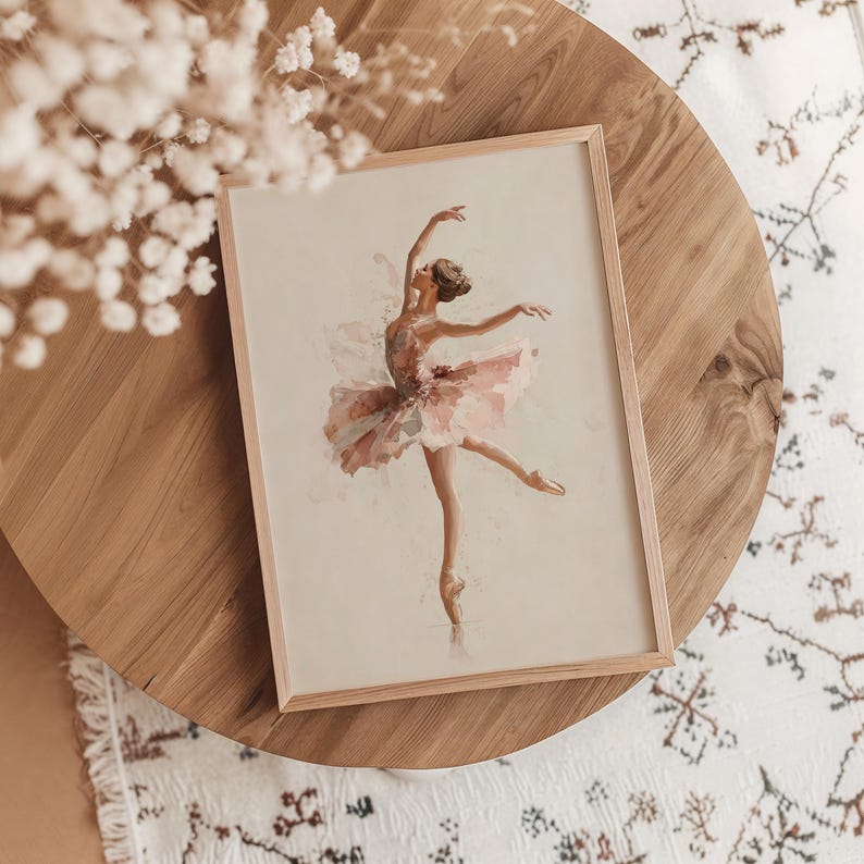 A delicate ballerina art print is framed in light wood, resting gracefully on an oak table, surrounded by subtle floral accents and a patterned rug, perfect for a pink nursery. The watercolor print adds a whimsical touch to a cozy kids room.