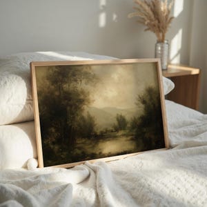 A serene vintage oil painting with moody landscape rests elegantly in a light wood frame, complementing the soft textures of a cozy farmhouse bed and the gentle glow from sunlit linens.