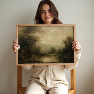 A serene vintage oil painting in a simple wooden frame held by a woman adds a touch of rustic wall art charm to this tranquil setting.