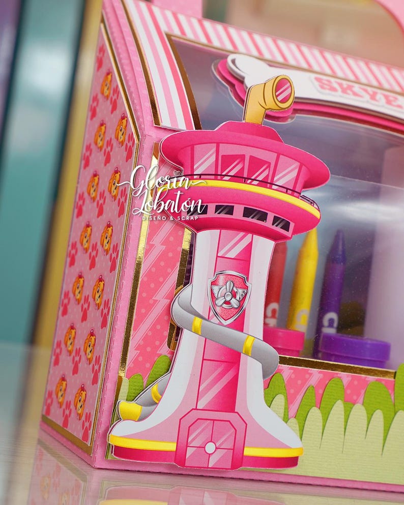 Pode incluir: Uma caixa de cart&atilde;o rosa e amarela com uma janela de pl&aacute;stico transparente. A caixa apresenta uma torre rosa e amarela com um logotipo de pata cinza e a palavra "Skye" no topo. A caixa &eacute; decorada com um padr&atilde;o de listras rosa e brancas e um padr&atilde;o de pegadas.