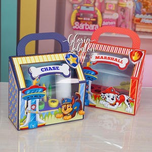 Pode incluir: Duas caixas de lembrancinhas com tema Patrulha Canina com janelas transparentes. A caixa azul apresenta Chase com seu carro de pol&iacute;cia e a caixa vermelha apresenta Marshall com seu caminh&atilde;o de bombeiros. Ambas as caixas t&ecirc;m uma al&ccedil;a e s&atilde;o decoradas com listras e pegadas de patas.