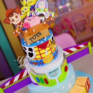 May include: A multi-tiered cake decorated with Toy Story characters. The cake features Woody, Buzz Lightyear, the Aliens, and Hamm the Pig. The cake has a Space Rangers theme with a light blue base and wooden toy blocks.
