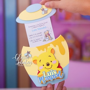 Puede incluir: Una tarjeta de invitación hecha a mano con el tema de Winnie the Pooh. La tarjeta es amarilla, azul y blanca, con un diseño recortado de un tarro de miel y una abeja. La invitación incluye el texto "Luis Manuel" y los detalles del evento.