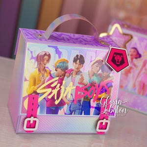 May include: A decorative box with a handle, featuring a group of animated characters and the text "Saja Boys." The box has a purple and pink color scheme, with a holographic handle and accents. A pink tag with a lion emblem hangs from the box.