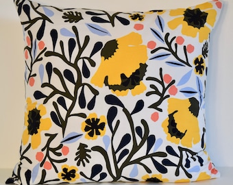 May include: A square throw pillow featuring a white background with a repeating botanical pattern. The design includes large yellow flowers with dark centers, dark green leafy branches, light blue leaves, and small coral pink circular accents.