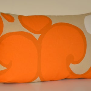 May include: Rectangular cushion featuring a beige background with large orange abstract shapes. A white shape is on the upper right corner. The cushion is a decorative item for a bed or sofa.