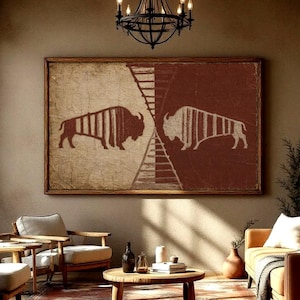 May include: A rectangular wall art piece featuring two mirrored bison silhouettes in white against a split background of beige and dark red, framed in wood. The artwork is centered above a living room seating area with chairs and a sofa.