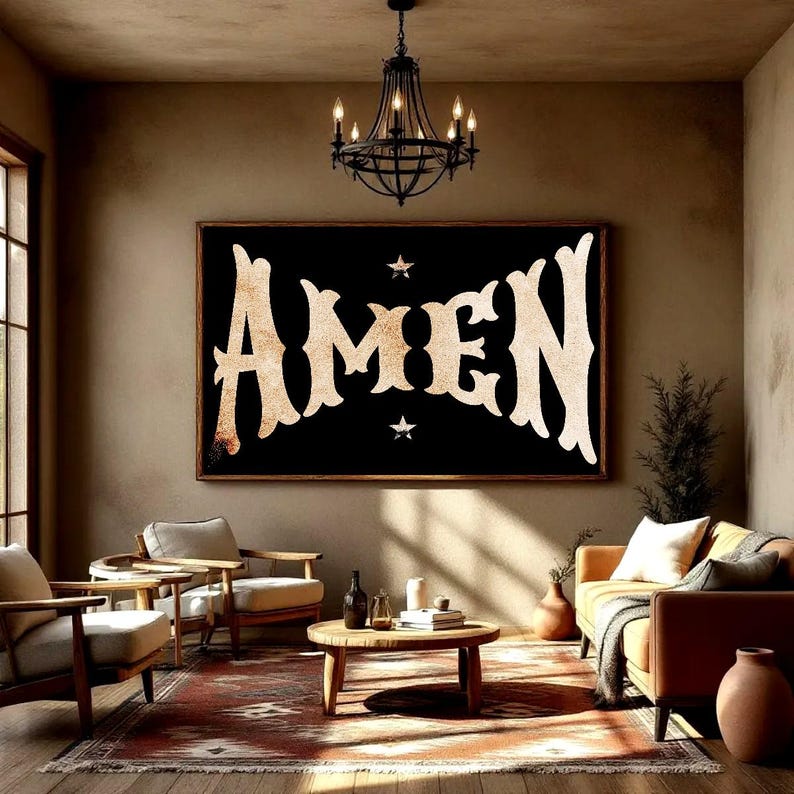 May include: A large framed artwork with the word "AMEN" in a vintage, ornate font. The letters are a light tan color against a black background, with two small stars. The artwork hangs above a seating area with a sofa, chairs, and a coffee table.