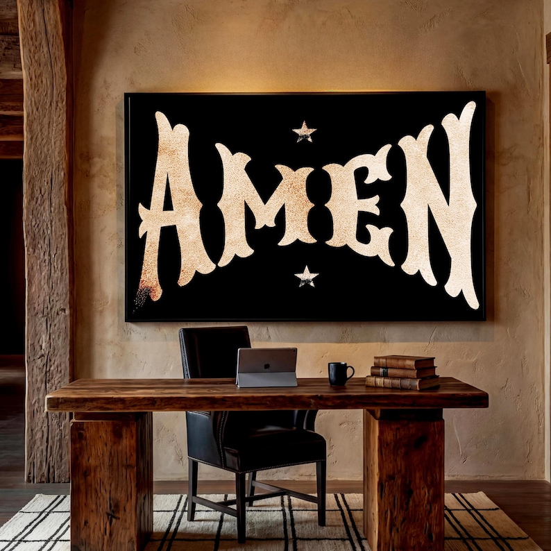 May include: A large black framed wall art with the word "AMEN" in a stylized, vintage font. Two small stars flank the text. The art hangs above a wooden desk with a black leather chair, a laptop, and books.