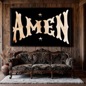 May include: A framed black wall art with the word "AMEN" in a vintage, ornate font. The artwork features two small star accents and is displayed above a floral patterned sofa on a white rug.