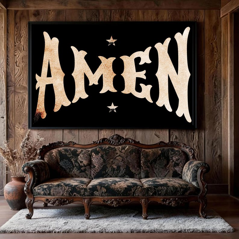 May include: A framed black wall art with the word "AMEN" in a vintage, ornate font. The artwork features two small star accents and is displayed above a floral patterned sofa on a white rug.