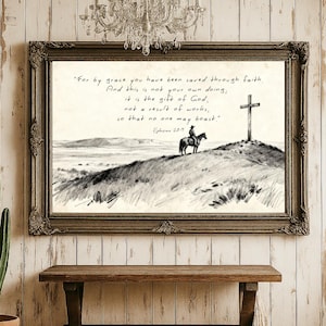 May include: A framed black and white print featuring a cowboy on horseback, a cross, and text from Ephesians 2:8-9. The print is in a decorative, ornate frame, and the background is a rustic wooden wall.