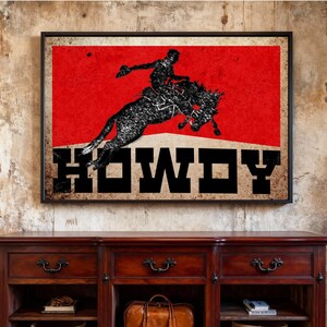 May include: Framed art print featuring a silhouette of a rodeo rider on a bucking bronco against a red background. The word "HOWDY" is displayed in bold, black letters. The artwork has a vintage, distressed look.