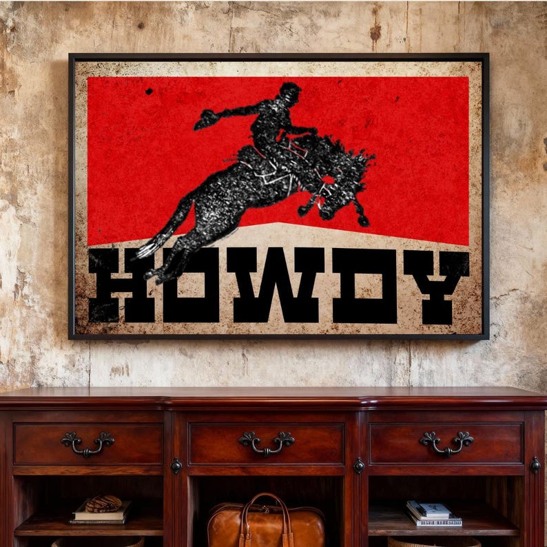May include: Framed art print featuring a silhouette of a rodeo rider on a bucking bronco against a red background. The word "HOWDY" is displayed in bold, black letters. The artwork has a vintage, distressed look.