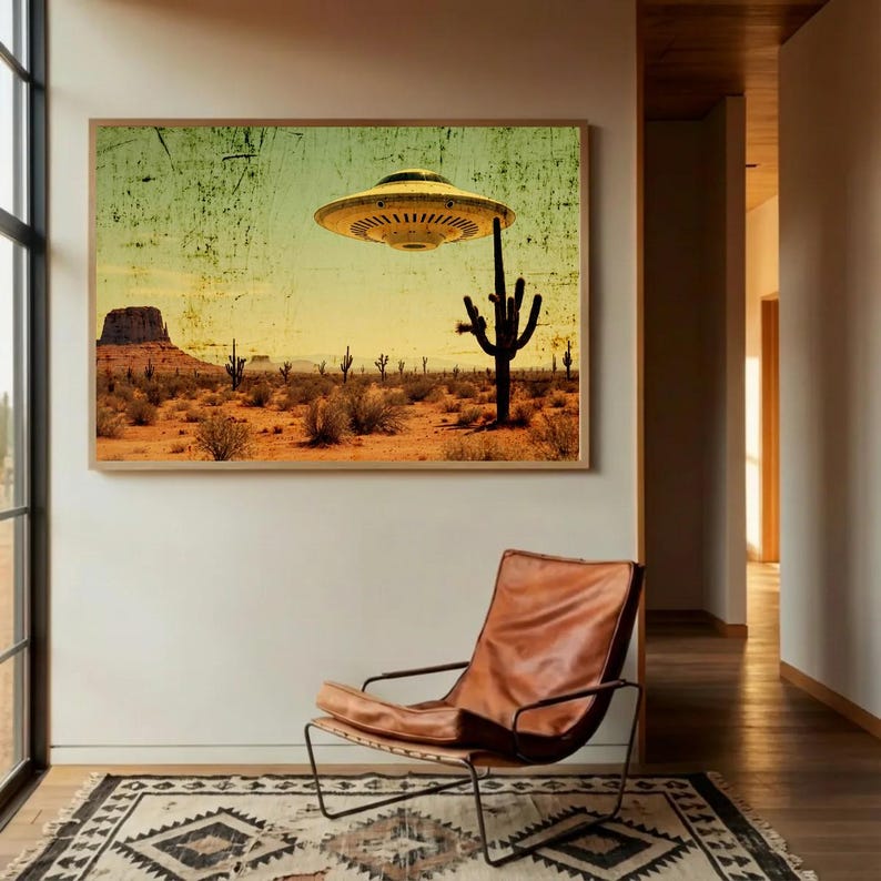 May include: A framed art print depicts a desert landscape with a vintage aesthetic. A yellow UFO hovers above a cactus. The scene includes a mesa, cacti, and desert vegetation under a yellow and green sky. A leather chair and patterned rug are in the foreground.