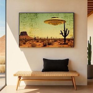 May include: A framed art print depicts a desert landscape with a vintage aesthetic. A yellow UFO hovers above cacti and a mesa. The artwork is displayed above a wooden bench with a black pillow, creating a Southwestern theme.