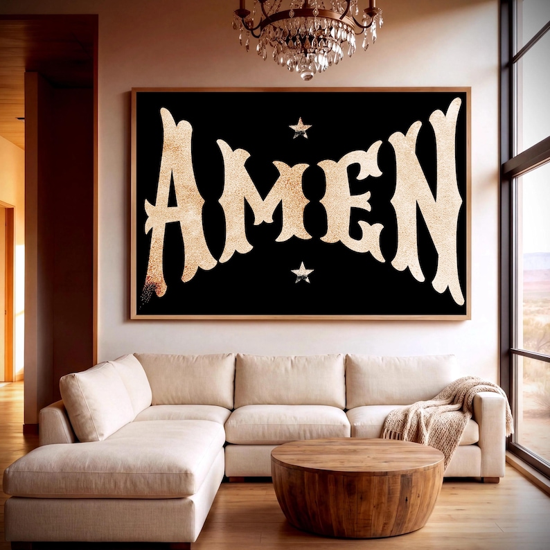 May include: A large framed artwork with the word "AMEN" in a gold glitter font against a black background. Two small gold stars are above and below the word. The artwork hangs above a cream-colored sectional sofa and a wooden coffee table.