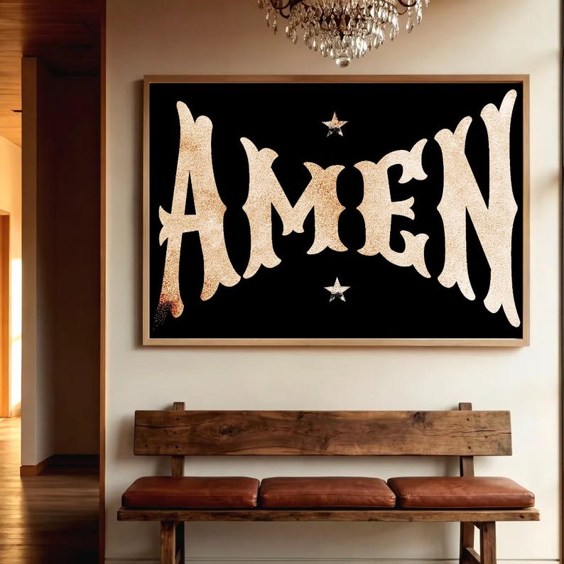 May include: A framed art print with the word "AMEN" in a gold, textured font against a black background. Two small star shapes are above and below the word. The artwork is displayed above a wooden bench with leather cushions.