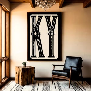 Könnte beinhalten: Ein gerahmtes Kunstwerk mit den Buchstaben "KY" in Schwarz und Weiß. Die Buchstaben sind mit dekorativen Elementen, darunter ein Stern, verziert. Das Kunstwerk hängt über einem schwarzen Ledersessel und einem Beistelltisch aus Holz.