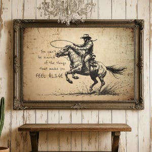May include: A framed sepia-toned wall art print featuring a sketch of a cowboy riding a horse while holding a lasso. The text reads: You can't be scared of the things that make you FEEL ALIVE. The artwork is enclosed in an ornate dark brown frame.