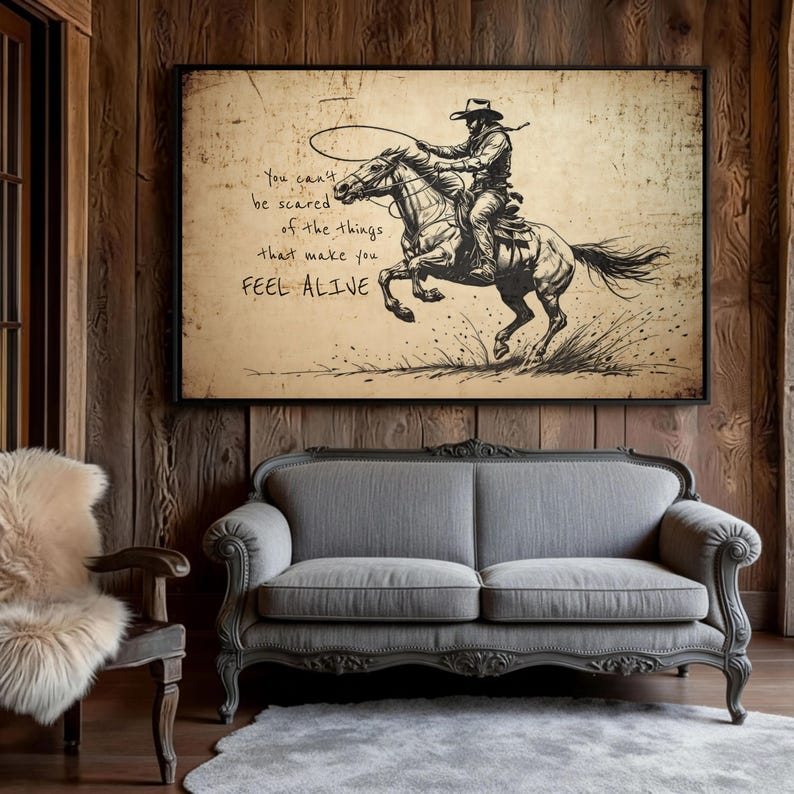May include: A rectangular wall art print featuring a black ink sketch of a cowboy riding a galloping horse while swinging a lasso. The background is a textured, aged beige paper. The text reads: You can't be scared of the things that make you FEEL ALIVE.