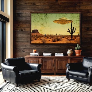 May include: A framed art print depicts a desert landscape with a hovering UFO. The artwork features a yellow-toned sky, cacti, and a mesa. The room includes black leather armchairs, a wooden cabinet, and a patterned rug.