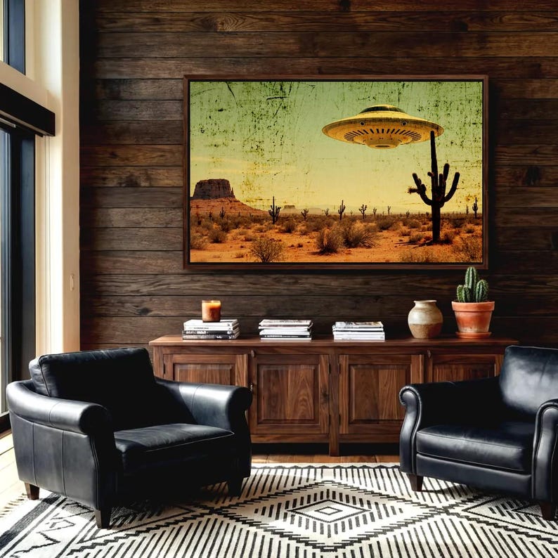 May include: A framed art print depicts a desert landscape with a hovering UFO. The artwork features a yellow-toned sky, cacti, and a mesa. The room includes black leather armchairs, a wooden cabinet, and a patterned rug.