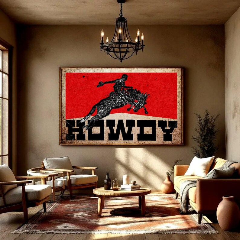 May include: A framed wall art piece featuring a rodeo cowboy riding a bucking bronco against a red background. The word "HOWDY" is displayed in bold, black letters. The artwork is displayed in a living room setting.