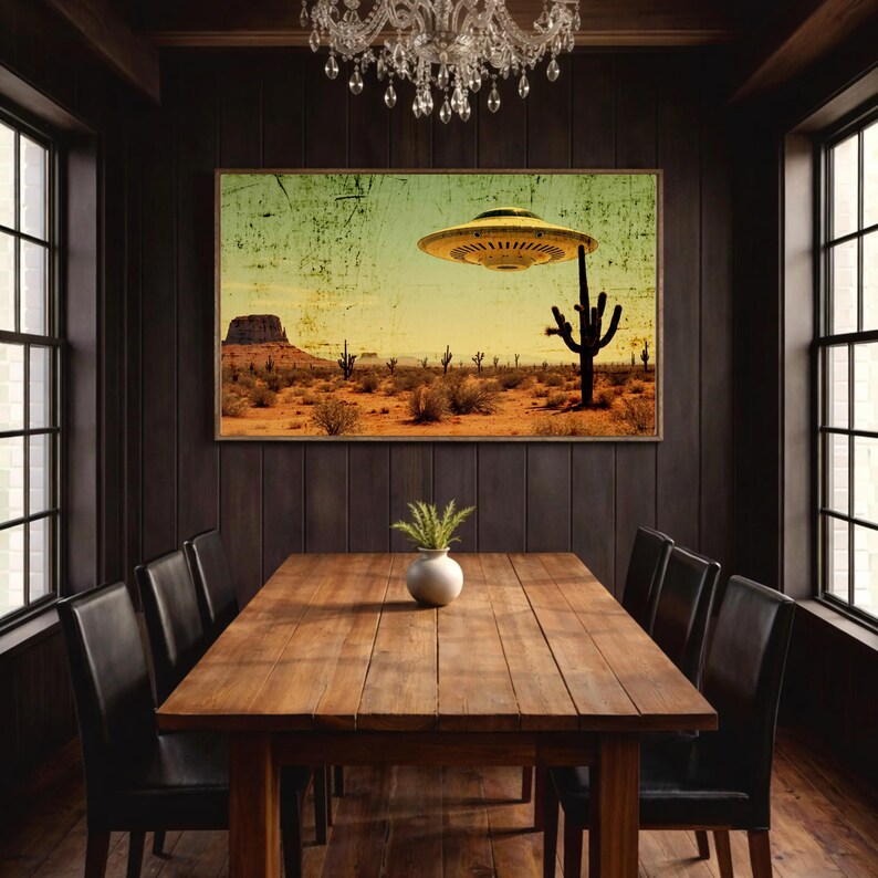 May include: A framed print depicting a desert landscape with a UFO hovering above a cactus. The artwork has a vintage, distressed look with a yellow and green sky. The print is displayed above a wooden dining table with black chairs.