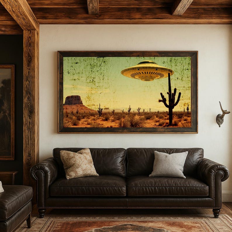 May include: A framed art print depicting a desert landscape with a vintage aesthetic. The artwork features a UFO hovering over cacti and mesas under a yellow and green sky. The print is displayed above a brown leather sofa.
