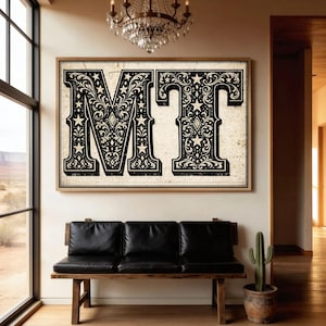 Könnte beinhalten: Große gerahmte Kunst mit den Buchstaben "MT" im Vintage-Stil. Die schwarzen Buchstaben sind mit floralen und Sternmustern auf cremefarbenem Hintergrund verziert. Das Kunstwerk hängt über einer schwarzen Lederbank in einem hellen Raum.