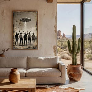 May include: A framed art print depicts cowboys saluting a UFO with a beam of light. The artwork has a vintage, distressed look with a brown wooden frame. The scene is set in a desert landscape, with a cactus in a terracotta pot and a view of the desert.