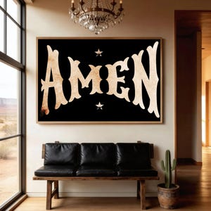 May include: A framed black wall art piece with the word "AMEN" in large, ornate, gold-colored letters. Two small star shapes are above and below the word. The artwork hangs above a black leather bench.