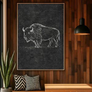 May include: A rectangular wall art print featuring a white line drawing of a bison on a dark charcoal gray textured background. The artwork is presented in a thin frame and depicts the animal in profile, showcasing its shaggy fur and horns.