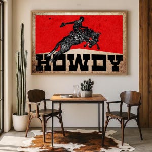May include: Framed wall art featuring a rodeo cowboy silhouette on a bucking bronco against a red background. The word "HOWDY" is displayed in bold, black letters. The artwork is displayed above a small wooden table and chairs.