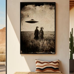 May include: A rectangular wall art print featuring a sepia-toned, vintage-style photograph of two figures wearing feathered headdresses standing in a field, looking up at a flying saucer hovering in the sky above them, framed in a thin black border.