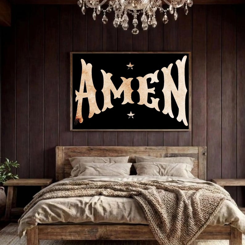 May include: A framed black wall art with the word "AMEN" in a vintage, stylized font. The artwork is centered above a wooden bed with neutral-toned bedding and a textured throw blanket. A chandelier hangs above the bed.