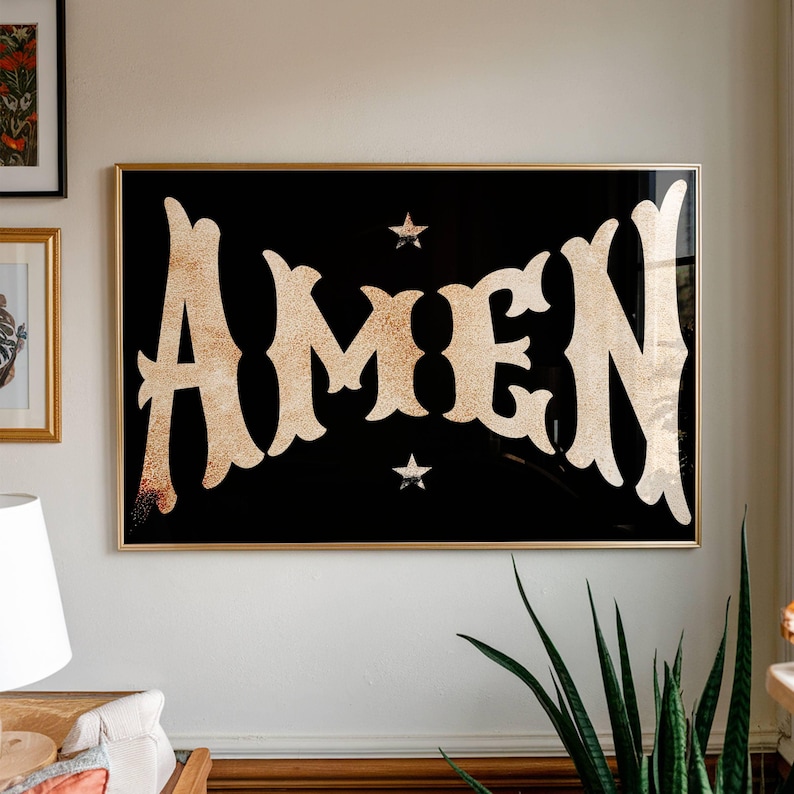 May include: A framed art print with the word "AMEN" in a gold, textured font against a black background. Two small gold stars are above and below the word. The frame is gold.