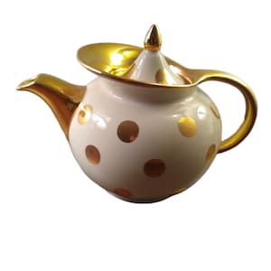 May include: A white teapot with gold polka dots and gold trim. The spout, handle, and lid are also gold. The lid has a small gold finial. The teapot is a classic shape and design.