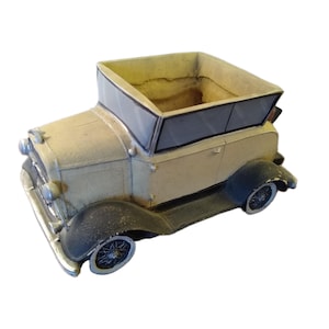 May include: A vintage-style car-shaped planter in cream and black. The planter has a rectangular opening, black fenders, and detailed wheels. The car's design evokes a classic, antique aesthetic, suitable for small plants or decorative items.