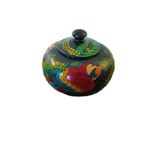 May include: A hand-painted, round wooden trinket box with a lid. The box is primarily black with colorful parrot designs in red, yellow, green, and blue. The lid has a small black knob.