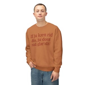 May include: A rust-colored sweatshirt with the text "/If ju kæn rid åls, ju dont nid glæ'slz/" in a darker shade. The sweatshirt is worn by a person in blue jeans.
