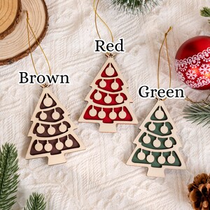 May include: Three wooden Christmas tree decorations in brown, red, and green, each with a gold string. The tree-shaped ornaments have cut-out details and are labelled with their colours: Brown, Red, and Green.