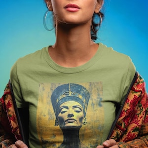 May include: A woman wearing a green t-shirt with a vintage-style image of an Egyptian queen wearing a headdress. The image is in shades of gold, blue, and black.